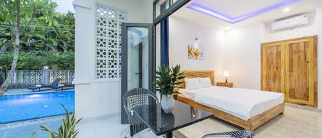 A modern bedroom with a glass door leading to a balcony, a wooden bed, and a small table with chairs.