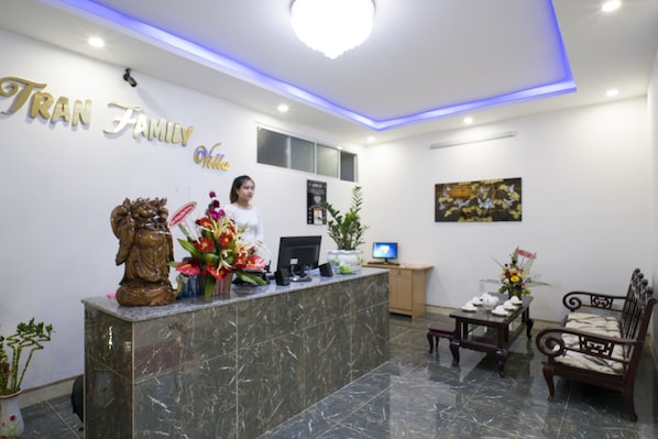 A reception area with a marble counter, a computer, and a seating area with a chair and a small table. - Tran Family Villas Boutique Hotel (Da Nang)