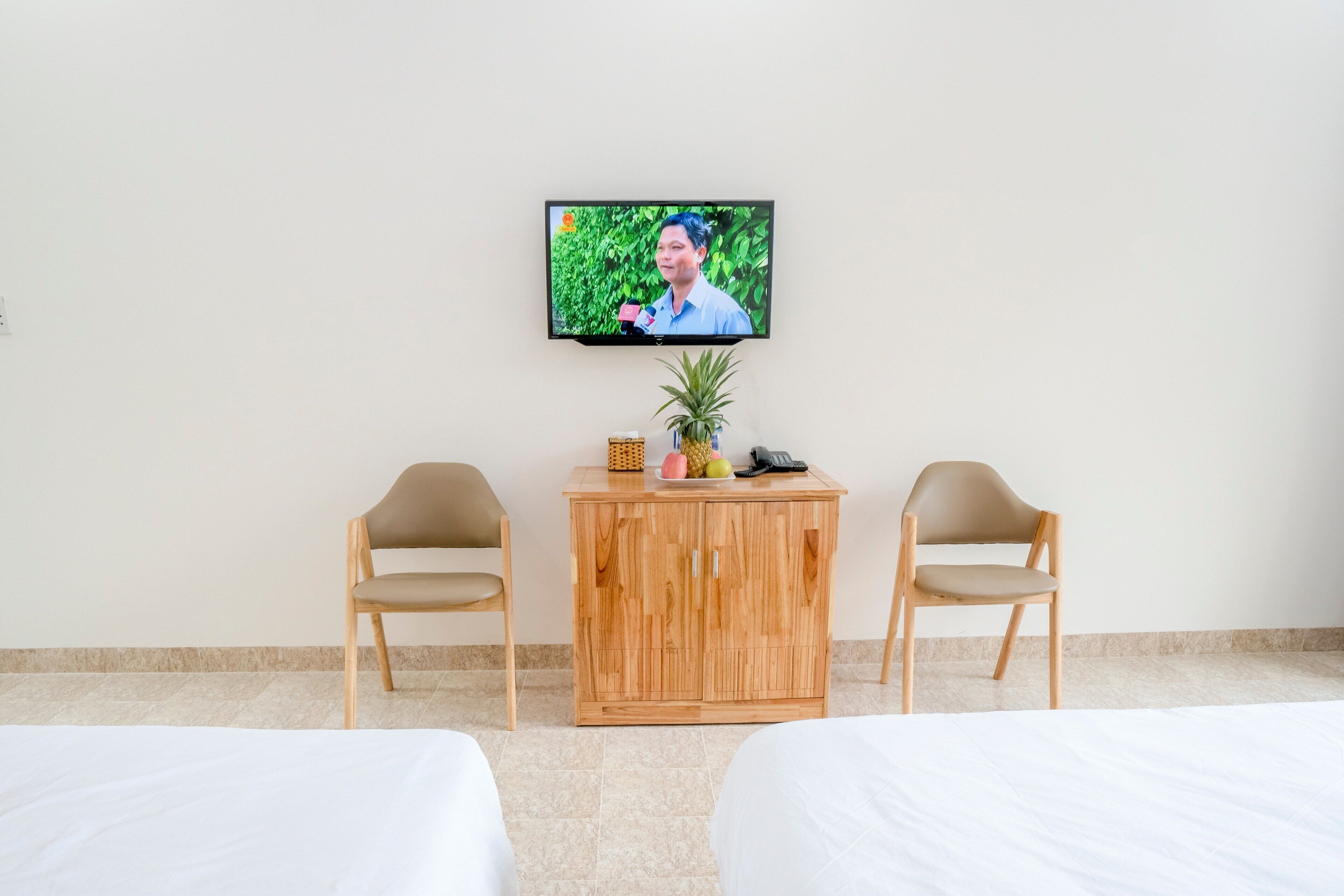 Habitación de hotel con dos camas, un armario de madera con un televisor montado en la pared y dos sillas.