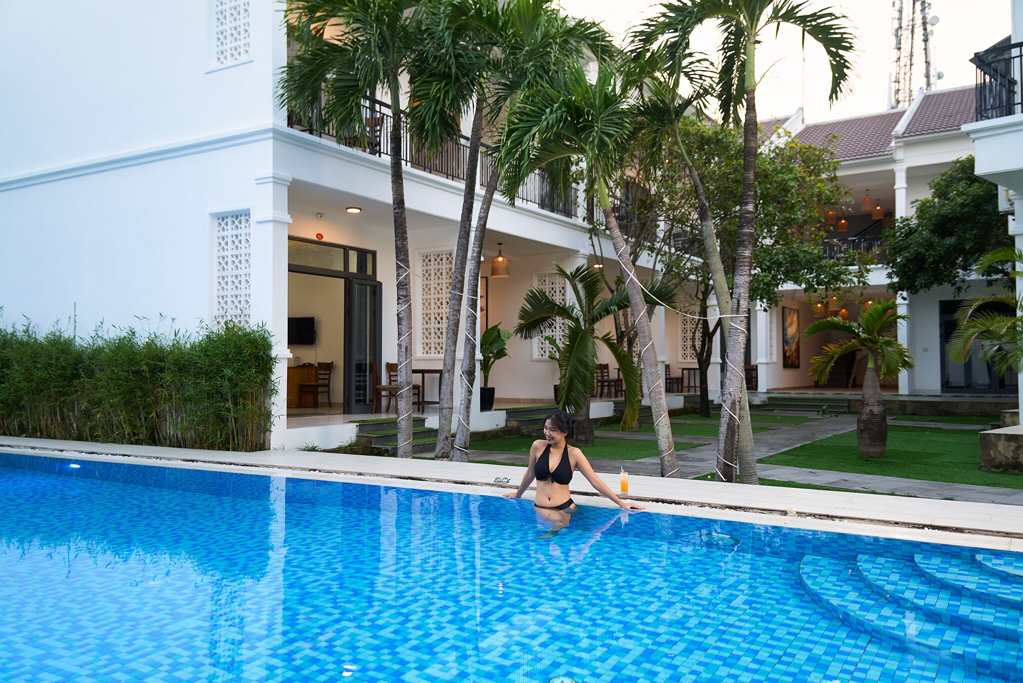 A woman sitting by a pool with a house in the background.