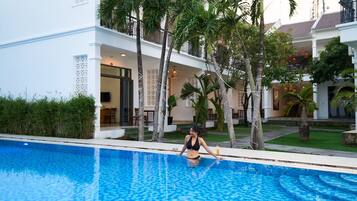 A woman sitting by a pool with a house in the background.