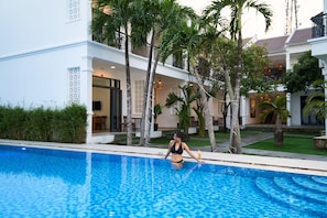 Una mujer sentada junto a una piscina, con una casa al fondo.