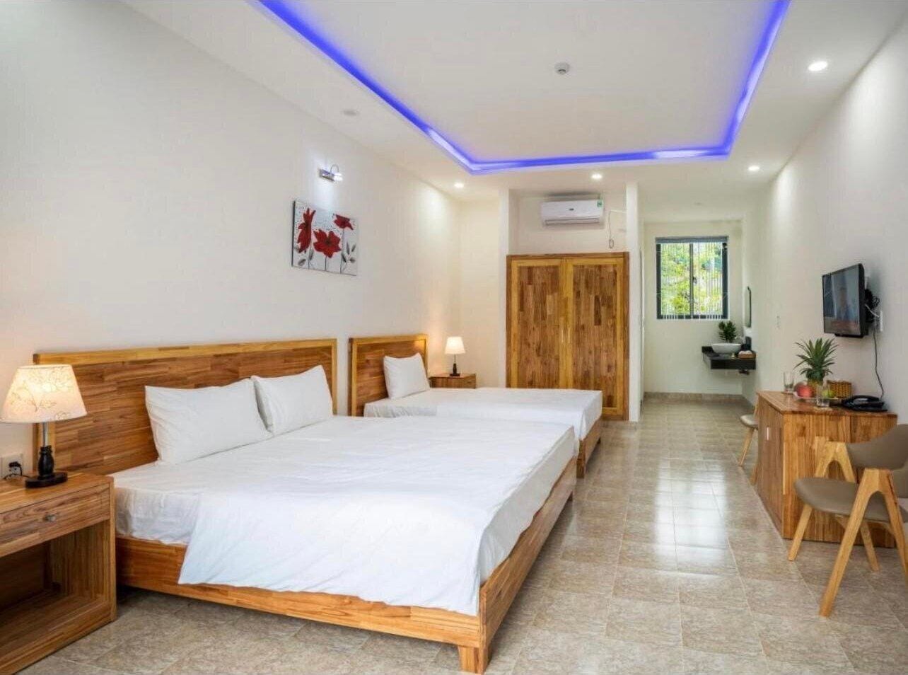 A modern bedroom with a large bed, bedside tables, a wooden wardrobe, a desk with a chair, and a TV.