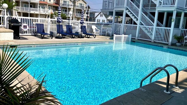 Una piscina cristallina blu circondata da una recinzione bianca e lettini da relax.