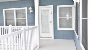 Una casa con un portico bianco, una porta bianca con il numero 203 e una ringhiera bianca.