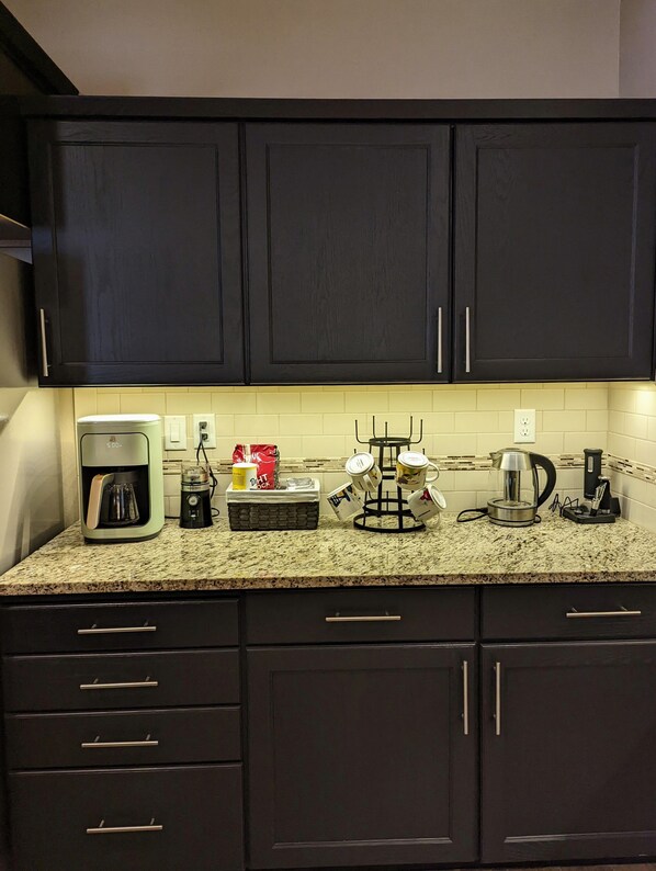A kitchen with dark cabinets, a coffee maker, a kettle, and a coffee grinder on the counter. - Spacious 3-bedroom home with outdoor space (Eugene)