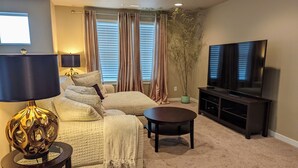 A living room with a beige sofa, a coffee table, a TV on a stand, and a lamp. - Spacious 3-bedroom home with outdoor space (Eugene)