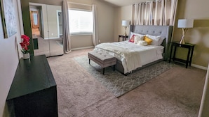 A bedroom with a bed, bedside tables, a nightstand, a bench, a window with curtains, and a door leading to another room. - Spacious 3-bedroom home with outdoor space (Eugene)