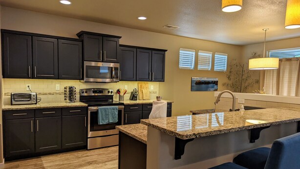 A modern kitchen with dark cabinets, a stainless steel microwave, a stove, and a granite countertop. - Spacious 3-bedroom home with outdoor space (Eugene)