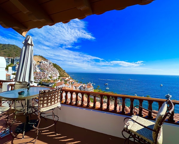 Una terraza con mesa y sillas, con vistas a un pueblo costero y al mar.