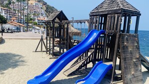 En lekplats på stranden med en blå rutschkana och lekanord i trä.