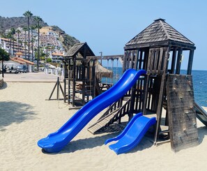 Ein Spielplatz am Strand mit einer blauen Rutsche und Holzspielgeräten.