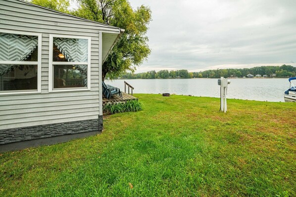 A house with a dock extending into a lake, surrounded by a grassy lawn and trees.