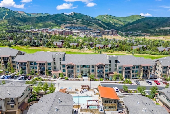 A modern hotel complex with multiple buildings, a swimming pool, and a view of surrounding mountains.