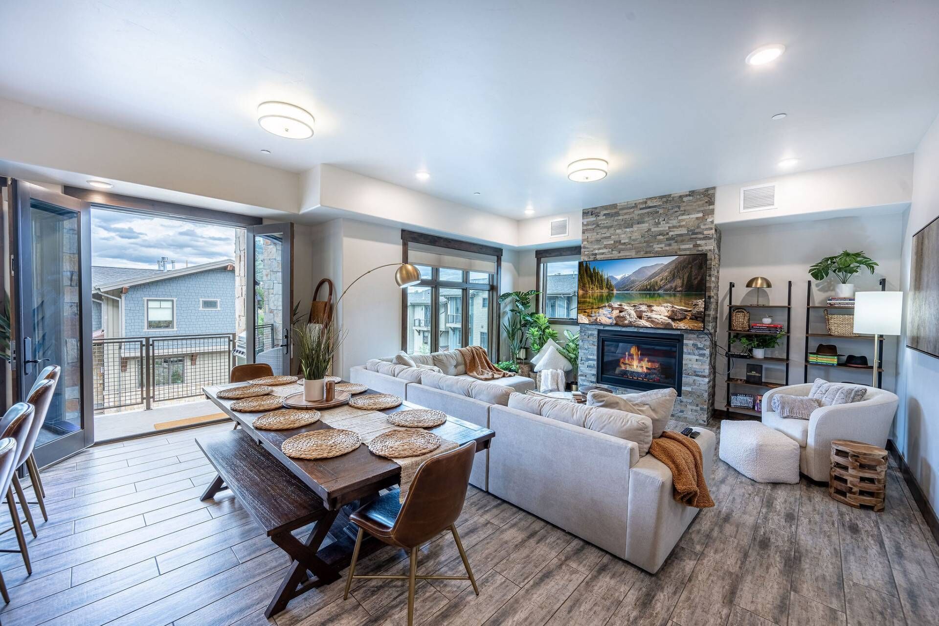 Amplia sala de estar con chimenea, comedor con mesa y sillas de madera, y balcón con vistas a casas vecinas.