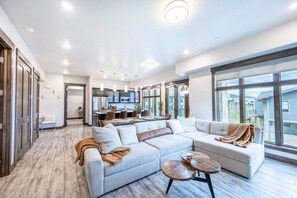 A spacious living area with a large sofa, a coffee table, and a view of the city through large windows. - Blackstone Flats 210 (Park City)