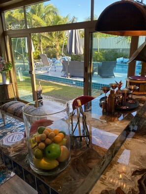 Enjoy a view of the pool area from the large window in this stylish room, featuring a marble floor and a glass table with a fruit bowl.