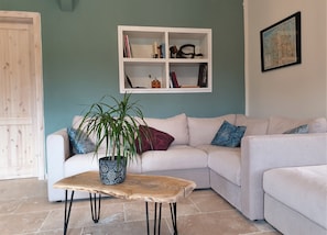 A living room with a white sofa, a wooden coffee table, a potted plant, and a white shelving unit against a teal wall. - 100-jähriges Fehnhaus an der Wieke mit Kamin (Großefehn)