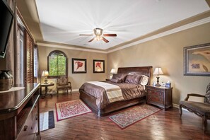 A bedroom with a large bed, two nightstands, a chair, a desk, and a ceiling fan.