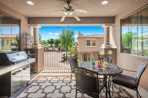 Une terrasse avec un barbecue, une table à manger et des chaises, donnant sur un quartier résidentiel.