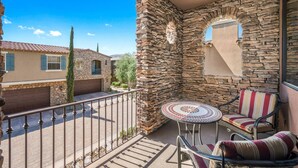 A balcony with stone walls, a small table, and two chairs. - Luxury Tuscan Condo in the Heart of Palm Desert! (Palm Desert)