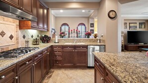 A kitchen with granite countertops, wooden cabinets, a stainless steel range hood, and a built-in dishwasher. - Luxury Tuscan Condo in the Heart of Palm Desert! (Palm Desert)