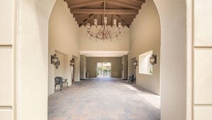 A spacious hallway with a stone floor, wooden ceiling beams, and wall-mounted lighting fixtures. - Luxury Tuscan Condo in the Heart of Palm Desert! (Palm Desert)