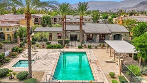 A residential area with a swimming pool, multiple houses with tiled roofs, and palm trees. - Luxury Tuscan Condo in the Heart of Palm Desert! (Palm Desert)