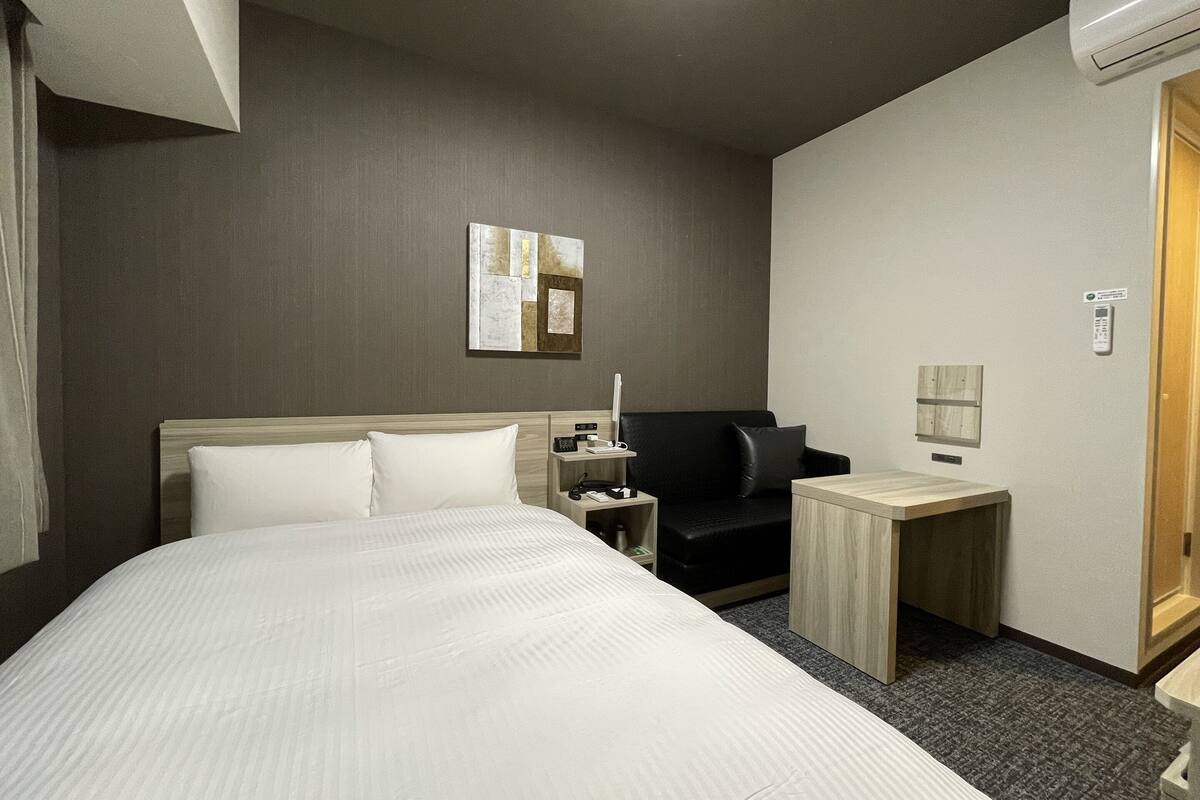 Una habitación de hotel con una cama grande, un escritorio, una silla, una mesita de noche, una lámpara y un cuadro en la pared.