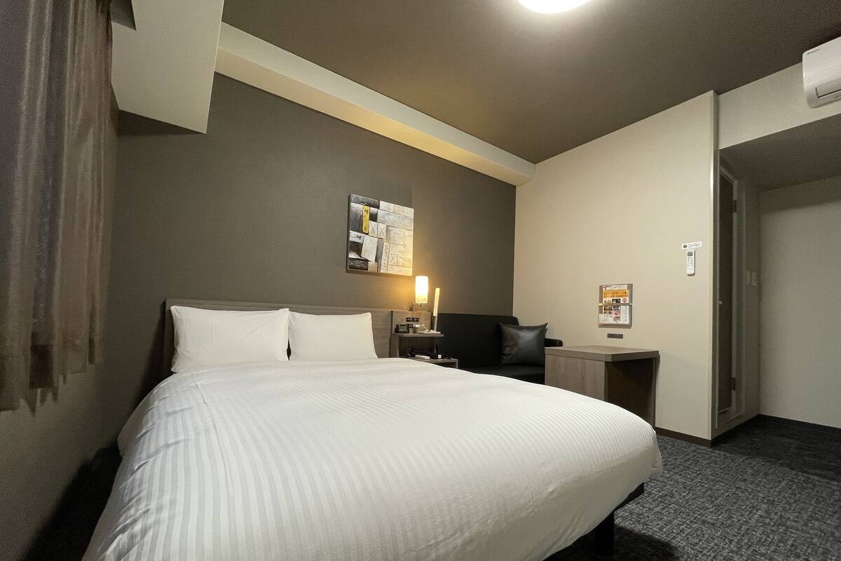 Habitación de hotel con una cama grande, un escritorio, una silla, una lámpara y una obra de arte colgada en la pared.