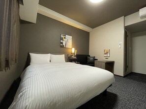 A hotel room with a large bed, a desk, a chair, a lamp, and a wall-mounted artwork.