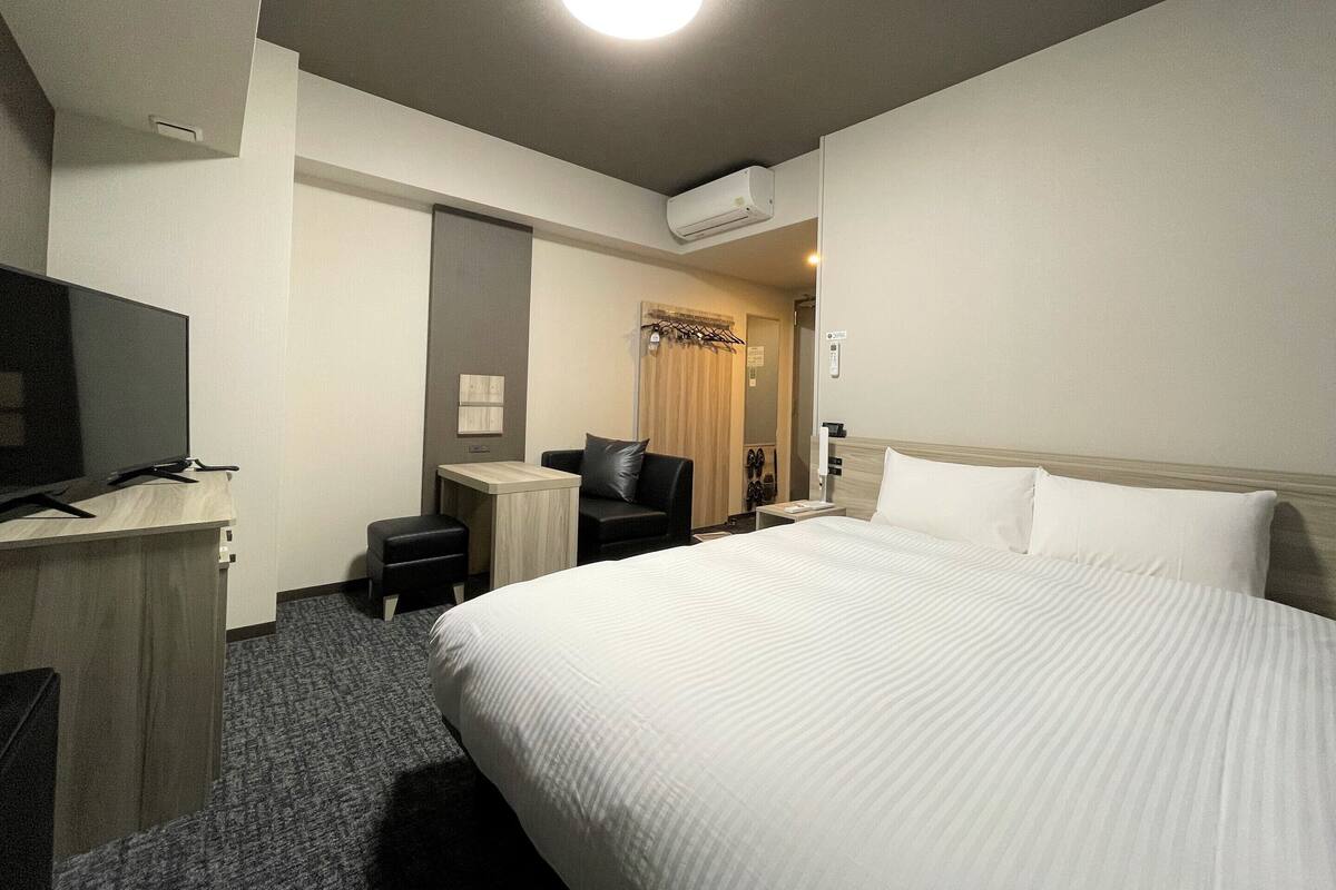 Una habitación de hotel con una cama grande, un escritorio con televisor, una silla y una mesita.