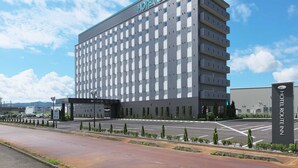 Un hotel moderno con un cartel con su nombre en la parte superior, un estacionamiento al frente y un cielo despejado.