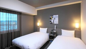 Habitación de hotel con dos camas, una mesita de noche, una lámpara, un cuadro en la pared y una ventana con cortinas.
