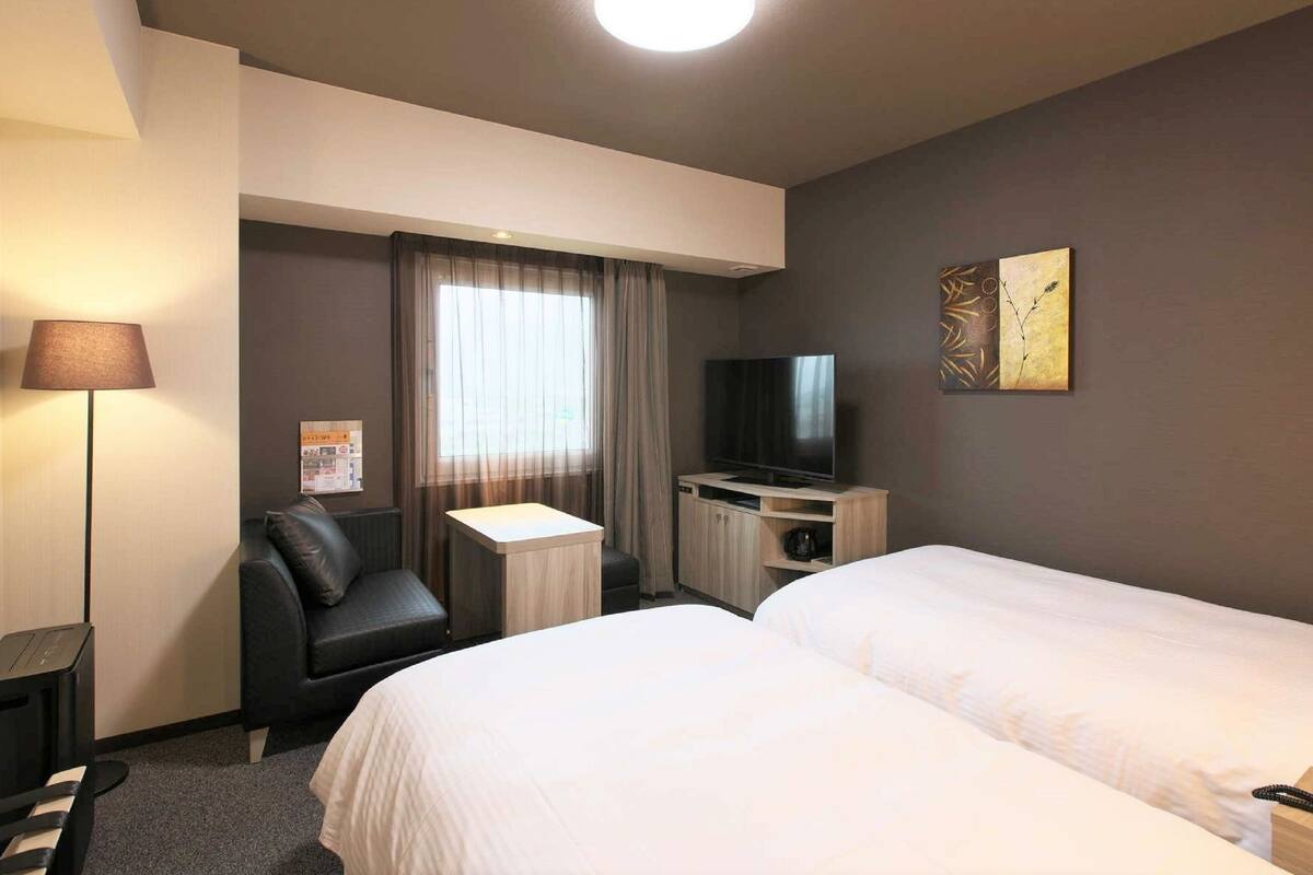 Habitación de hotel con dos camas, televisión, escritorio, lámpara y ventana con cortinas.