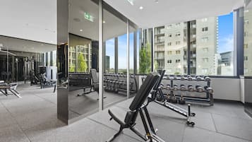 Un gimnasio moderno con diversos equipos de ejercicio, amplias ventanas que ofrecen vistas a un paisaje urbano y un interior limpio y bien iluminado.