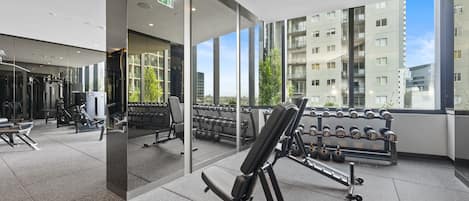 A modern gym with various exercise equipment, large windows offering views of a cityscape, and a clean, well-lit interior.