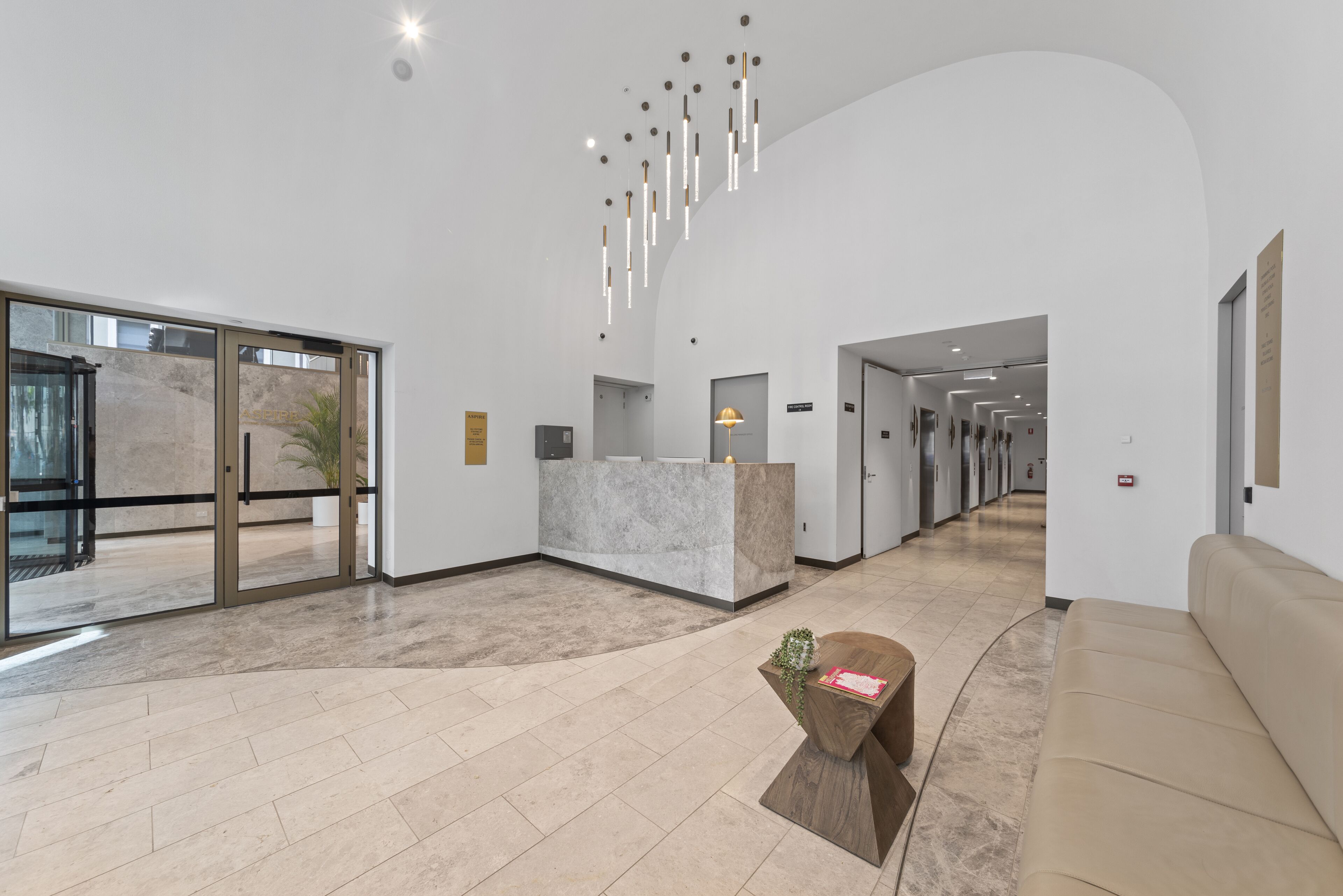 A modern lobby with a reception desk, a seating area, and a hallway leading to other rooms.