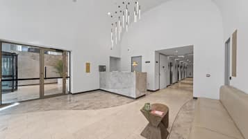 A modern lobby with a reception desk, a seating area, and a hallway leading to other rooms.