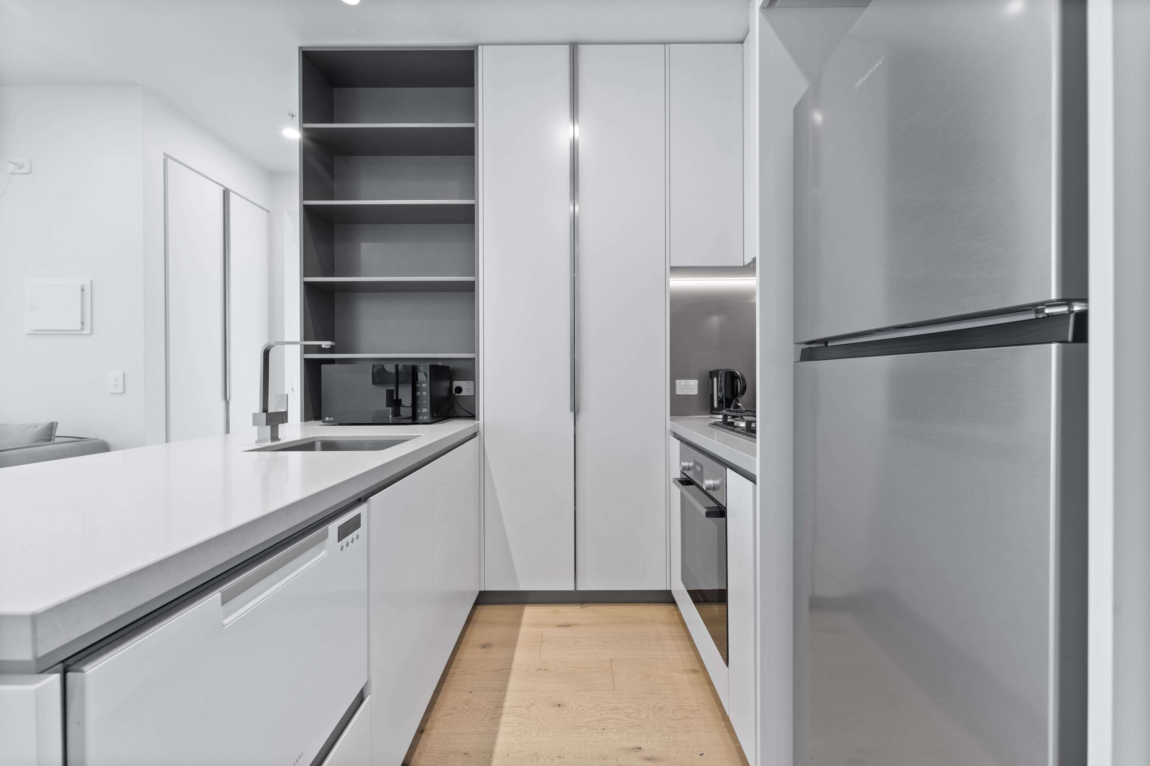 A modern kitchen with white cabinetry, a stainless steel refrigerator, and a built-in oven.