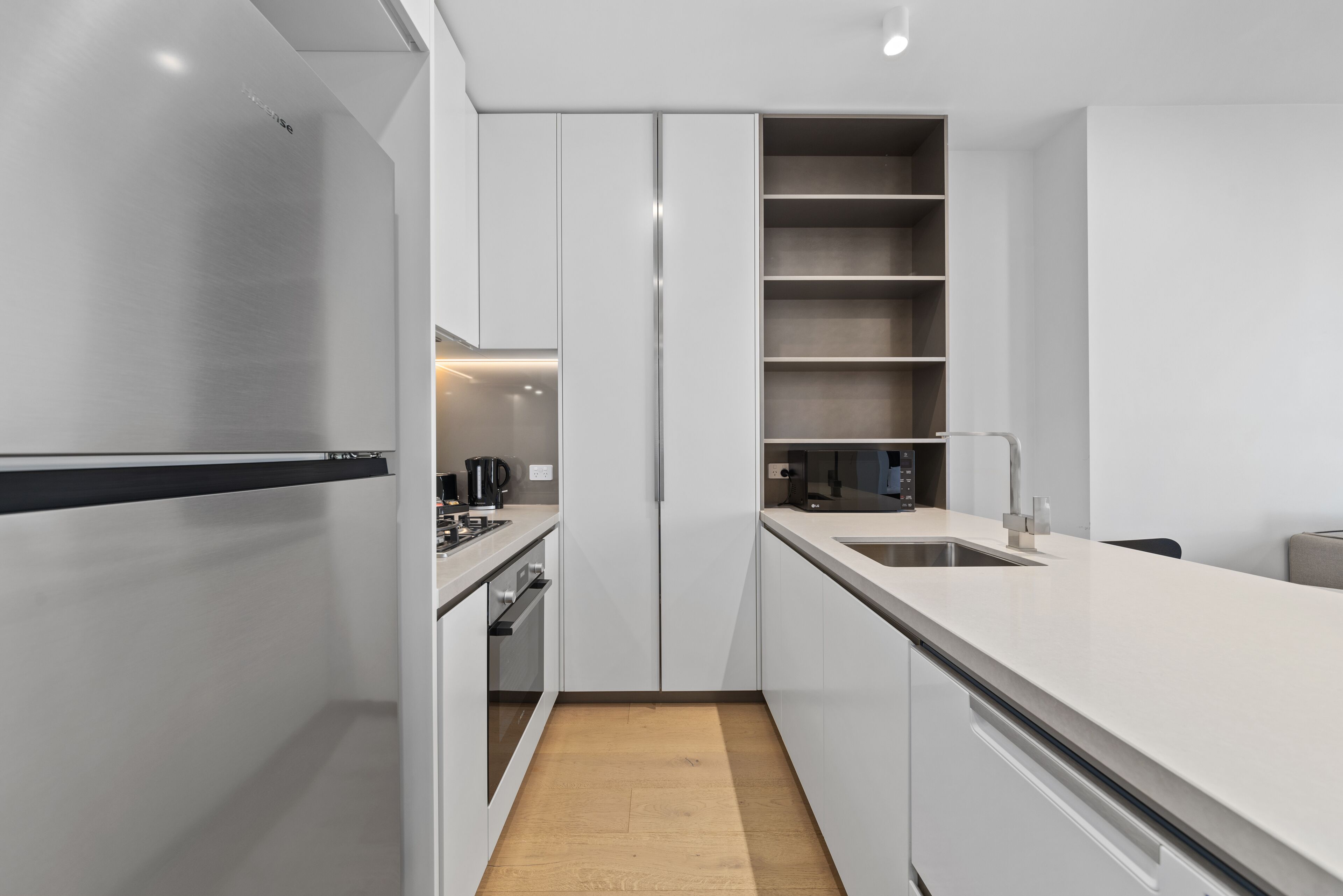 Une cuisine moderne avec des meubles blancs, un réfrigérateur en acier inoxydable, un four encastré et un plancher en bois.