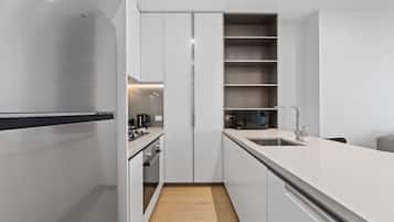 Une cuisine moderne avec des meubles blancs, un réfrigérateur en acier inoxydable, un four encastré et un plancher en bois.