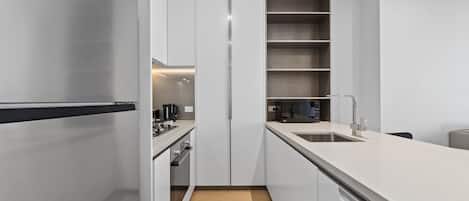 A modern kitchen with white cabinetry, a stainless steel refrigerator, a built-in oven, and a wooden floor.