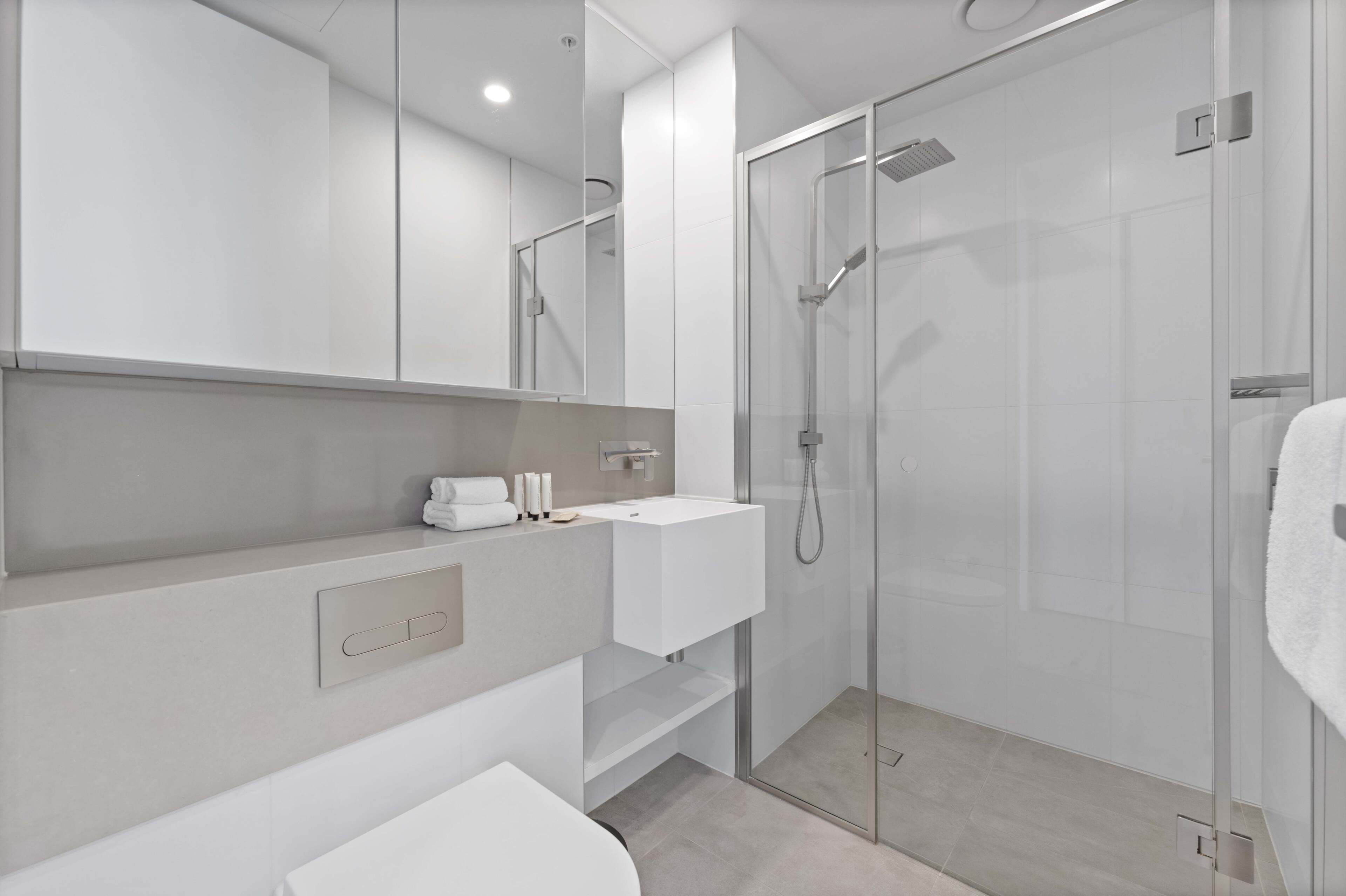 A modern bathroom with a glass-enclosed shower, a white sink, and a large mirror.
