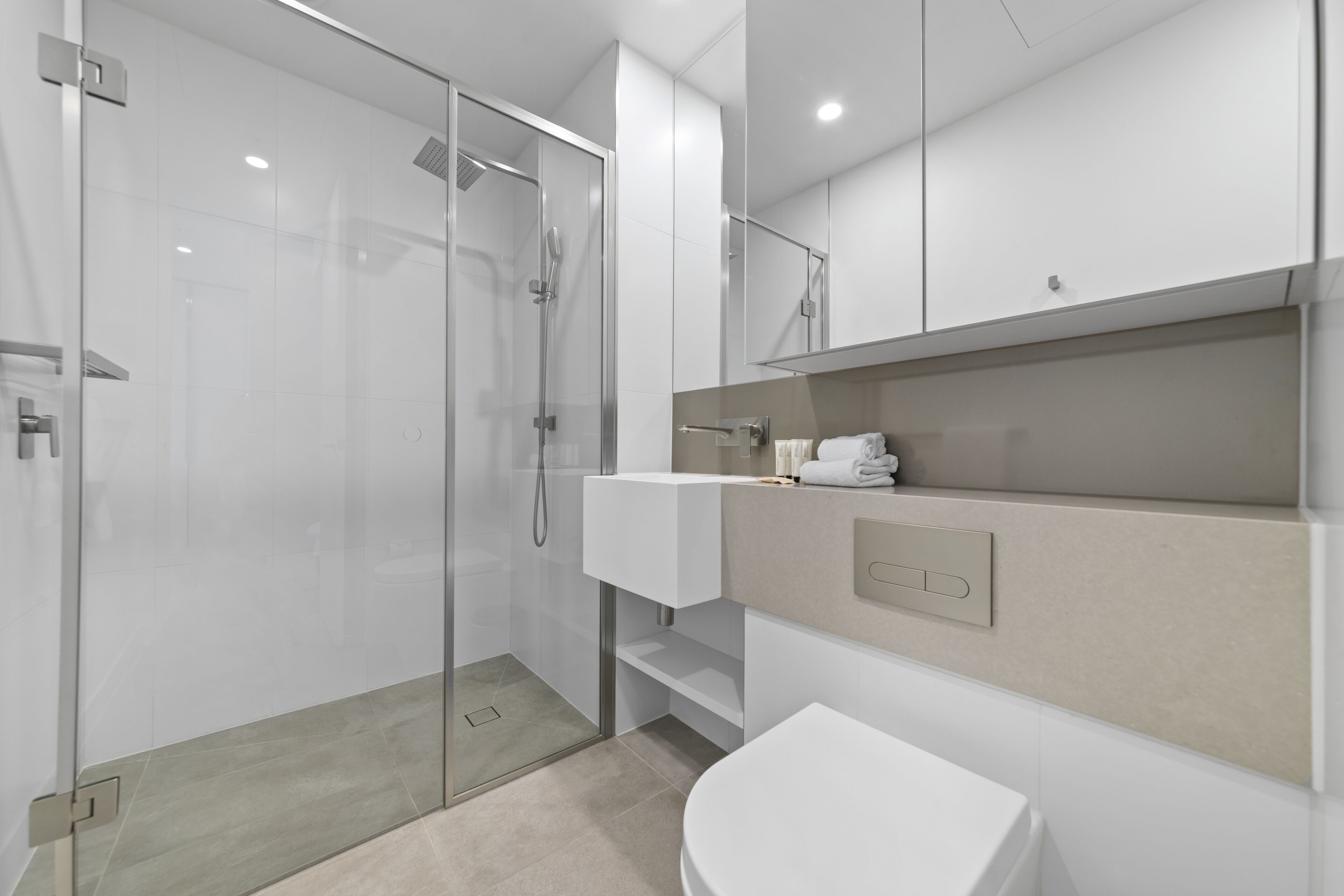 A modern bathroom with a glass-enclosed shower, a white sink, and a beige countertop.