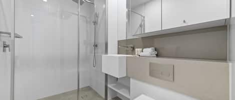 Un baño moderno con ducha acristalada, lavamanos blanco y encimera color beige.