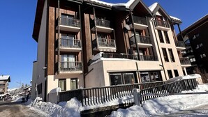 A multi-story hotel with balconies, a snow-covered ground, and a clear blue sky. - Studio for 4 near shops, 450 m to slopes (Les Carroz d'Arâches)