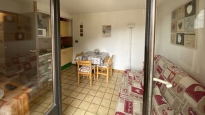 A dining area with a table and chairs, a kitchen in the background, and a sofa with a heart pattern. - Studio for 4 near shops, 450 m to slopes (Les Carroz d'Arâches)