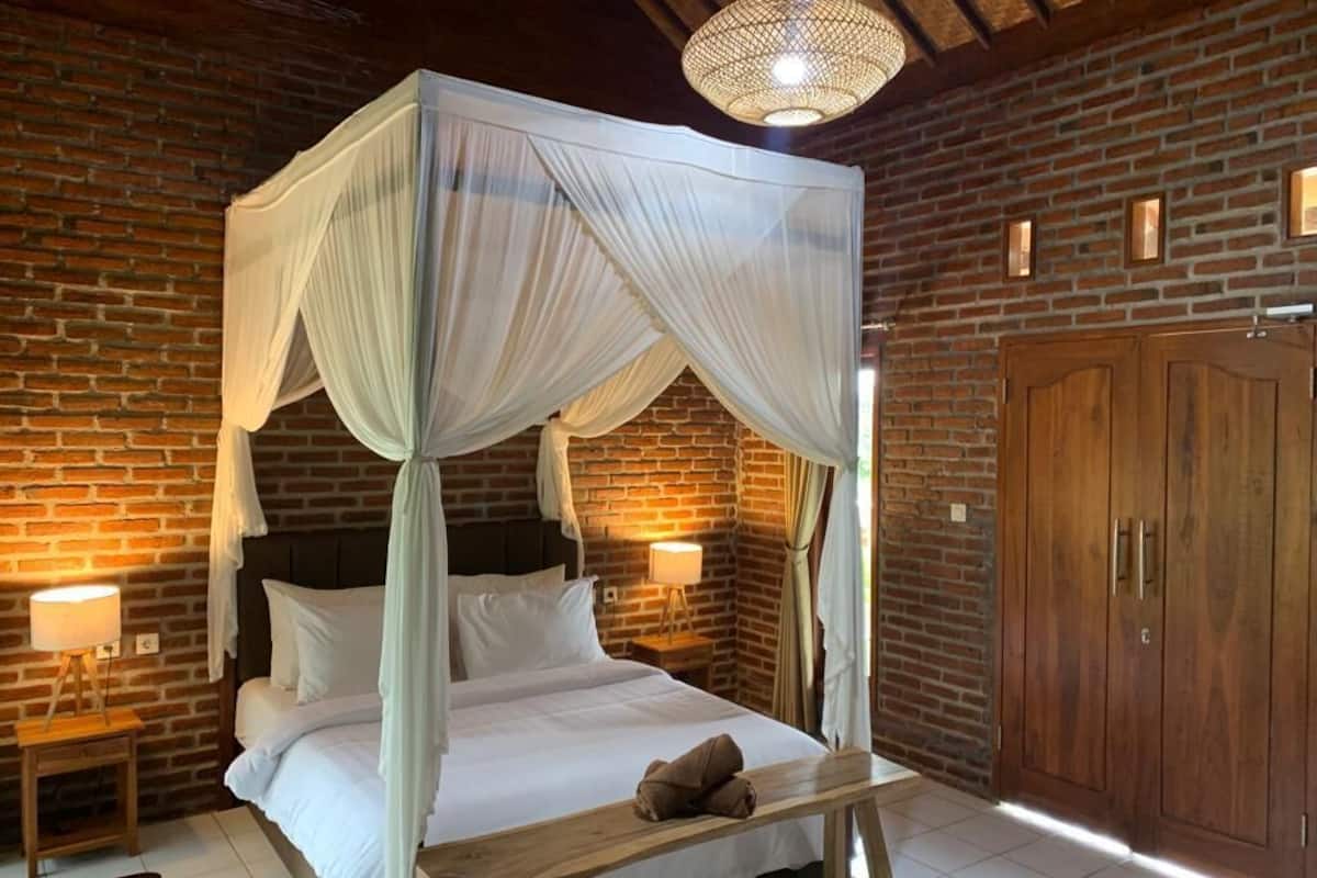 Un lit à baldaquin à quatre poteaux avec du linge de lit blanc, une table de chevet en bois avec une lampe et une grande armoire en bois.