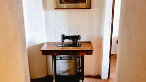 Un pasillo estrecho con una máquina de coser sobre una mesa de madera, un cuadro enmarcado en la pared y una puerta a la derecha.